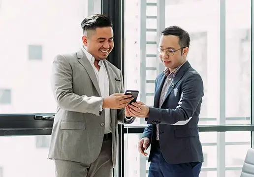 A photo of two colleagues in an office looking at a cellphone