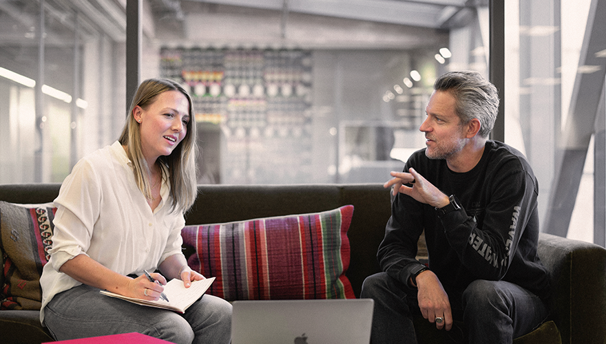 Two Caucasian colleagues sitting on couch and talking.