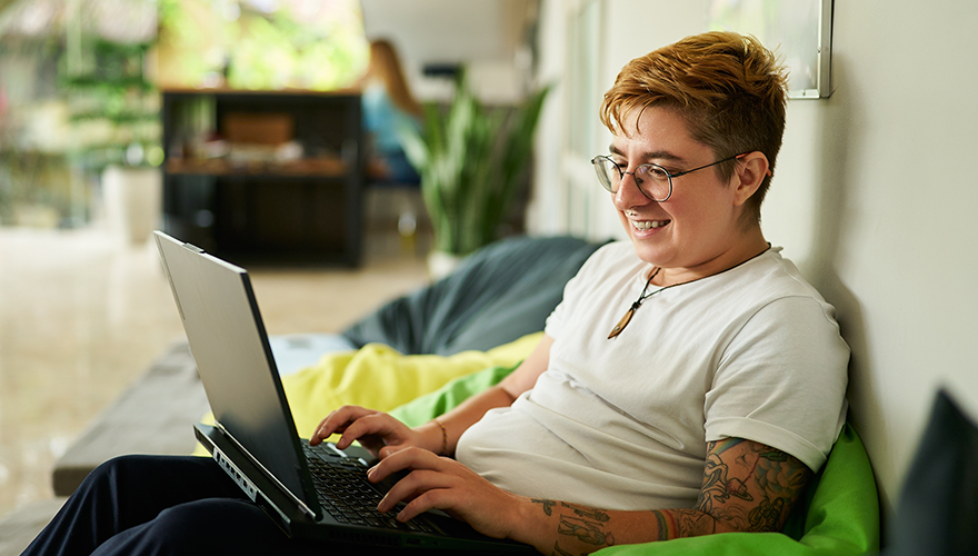 A tattooed person on their laptop smiling while working from home