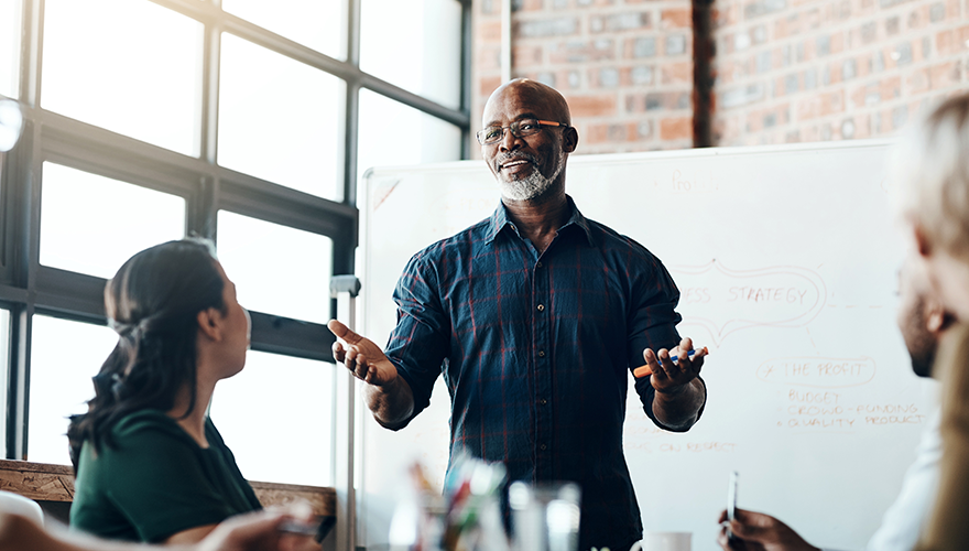 A man standing up speaking to everyone in a workplace setting