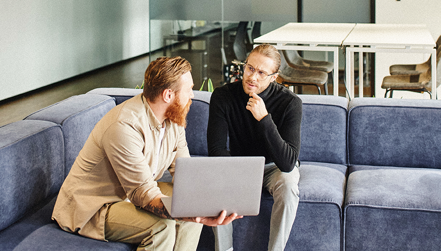 Two men sitting on couches and working on a laptop