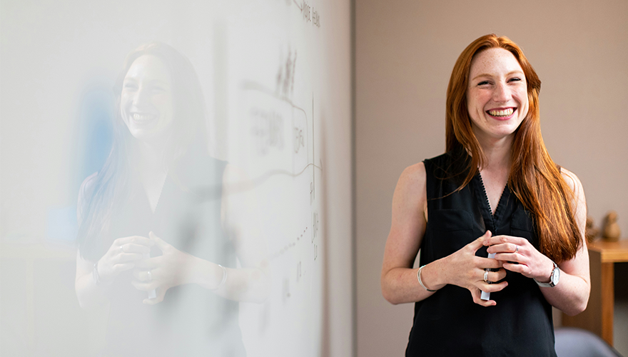 Photo of a smiling woman standing proudly next to a whiteboard