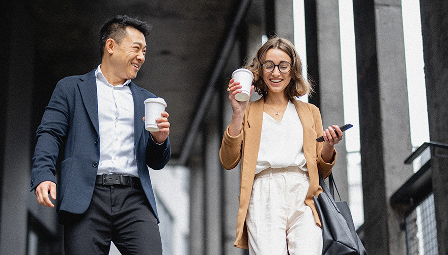 Two coworkers holding coffee and walking outside